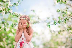 Adorable little girl enjoying smell in a flowering cherry spring garden photo