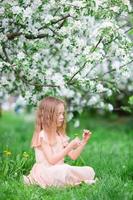 adorable niñita disfrutando del día de primavera en un jardín floreciente de manzanas foto