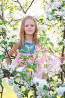 adorable niñita disfrutando del día de primavera en un jardín floreciente de manzanas foto