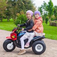 Two Little beautiful sisters sitting on toy motorcycle in green park photo