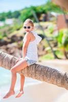 adorable niñita en una playa tropical sentada en una palmera durante las vacaciones de verano foto
