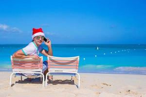joven con sombrero de navidad en la silla de playa foto