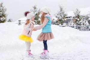 Adorable girls skating on ice rink outdoors in winter snow day photo