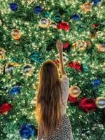 niña en el fondo del árbol de navidad en miami. hermoso árbol de navidad en la zona popular en la víspera de navidad y luces foto