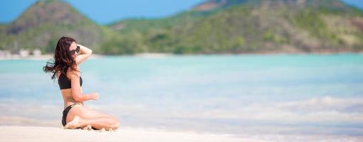 Woman sitting on beach laughing and enjoying summer holidays looking at the camera. Beautiful model in bikini sitting down. photo