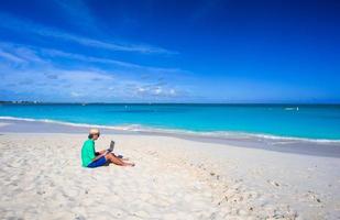 Young man working on laptop at tropical beach photo