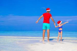 Happy father and his adorable daughter in Santa Hat at tropical beach photo