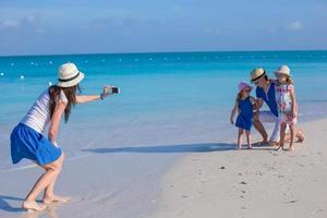 joven madre haciendo fotos en el teléfono de su familia en la playa