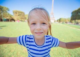 Adorable little girl taking selfie by phone near the Eiffel tower outdoors photo