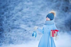 adorable chica con lámpara y caja de regalo de navidad en invierno en la víspera de navidad al aire libre foto