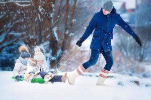 Little girls enjoying sledding. Father sledding his little adorable daughters. Family vacation on Christmas eve outdoors photo