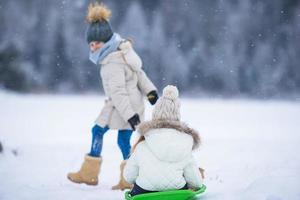 Little adorable girls enjoy a sleigh ride. Child sledding. Children play outdoors in snow. Family vacation on Christmas eve outdoors photo