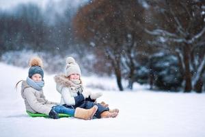 Little adorable girls enjoy a sleigh ride. Child sledding. Children play outdoors in snow. Family vacation on Christmas eve outdoors photo