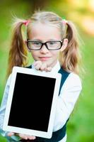 Adorable little girl holding tablet PC outdoors in autumn sunny day photo