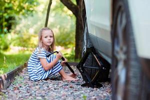 Adorable little girl changing a car wheel outdoors on beautiful summer day photo