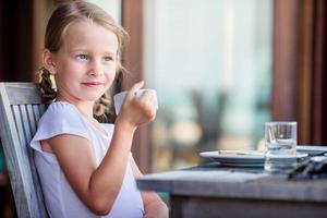 adorable niña desayunando con té en un café al aire libre foto