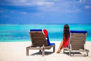 Two loungers with red Santa Hats on tropical white beach with turquoise water. Young woman enjoy beach vacationbeach photo