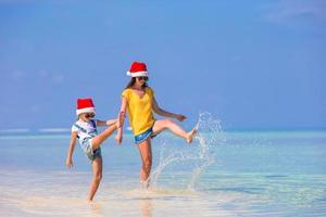 niña y madre joven con sombreros de santa durante las vacaciones en la playa foto