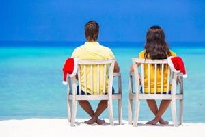 Young couple in Santa hats relaxing on tropical beach during Christmas vacation photo