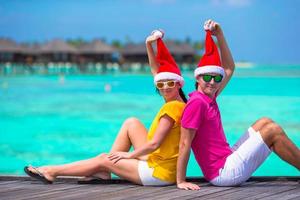 pareja joven con sombreros de santa relajándose en la playa durante las vacaciones de navidad foto