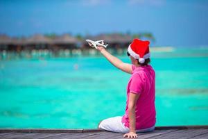 Young man in santa hat on white beach with miniature of airplane photo