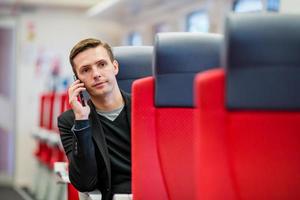 Young caucasian guy traveling by train. Tourist writing a message on cellphone while traveling by express train photo