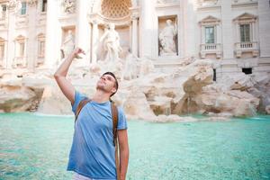 hombre feliz turista tirando monedas en la fuente de trevi, roma, italia para la buena suerte. chico caucásico deseando volver. foto