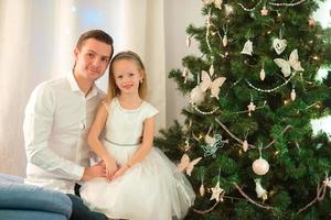 padre abraza a su hija cerca del árbol de navidad en la víspera de navidad foto