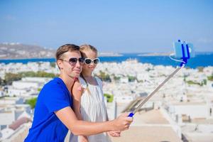 Family vacation in Europe. Father and daughter taking selfie background Mykonos town in Greece by their smartphone photo