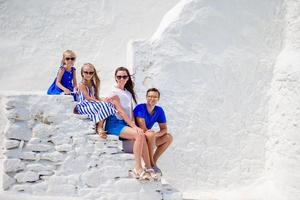 Family vacayion in Europe. Parents and kids at street of typical greek traditional village with white walls and colorful doors on Mykonos Island, in Greece photo