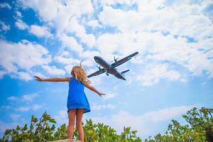 Adorable little child girl looking to the sky and flying plane directly above her. Beautiful exciting picture photo