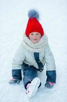 Little adorable girl sitting on ice with skates after fall photo