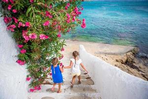 Two girls in blue dresses having fun outdoors. Kids at street of typical greek traditional village with white walls and colorful doors on Mykonos Island, in Greece photo