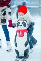 Little adorable girl learning to skate on ice rink outdoor photo