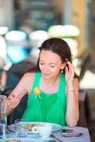 Young woman eating spaghetti at outdoor cafe on italian vacation photo