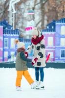 Little adorable girl skating on ice-rink with mother photo