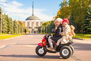 Two Little beautiful sisters sitting on toy motorcycle in autumn park photo