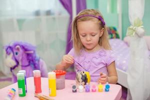 Little beautiful girl draws paints on the table photo