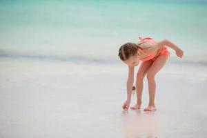 Adorable little girl drawing on white sand at the beach photo