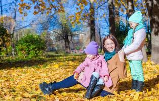 Two adorable girls with his young mom in the park on a sunny autumn day photo