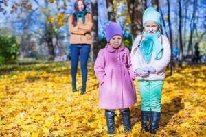 Two adorable girls with his young mom in the park on a sunny autumn day photo
