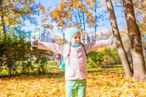Little funny girl throws autumn leaves in park on fall day photo