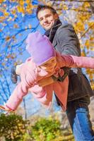 adorable niñita con padre feliz divirtiéndose en el parque de otoño en un día soleado