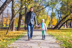 adorable niñita con padre feliz caminando en el parque de otoño en un día soleado foto