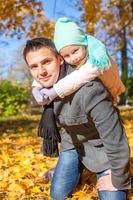 adorable niñita con padre feliz divirtiéndose en el parque de otoño en un día soleado