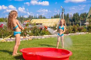 Two little sisters frolicing, splashing and having fun in their yard photo