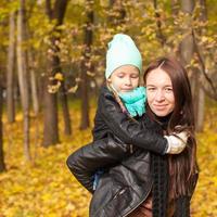 Happy mother and her cute daughter walking in yellow autumn forest on a warm sunny day photo