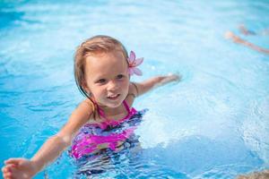 Little cute happy girl with flower behind her ear has fun in the swimming pool photo