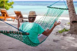 joven sentado en el sombrero en la posición de loto en la hamaca foto