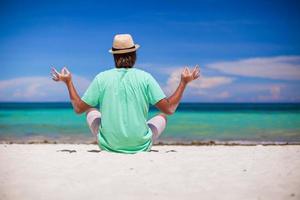 Young man sitting in lotus position on white sand beach photo